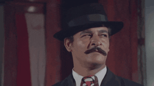 a man with a top hat and mustache looks at the camera