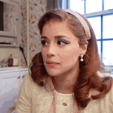 a woman with red hair is wearing a headband and earrings while sitting in front of a window .