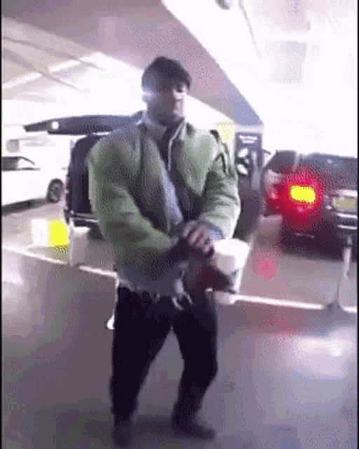 a man in a green jacket is holding a cup of coffee in a parking garage
