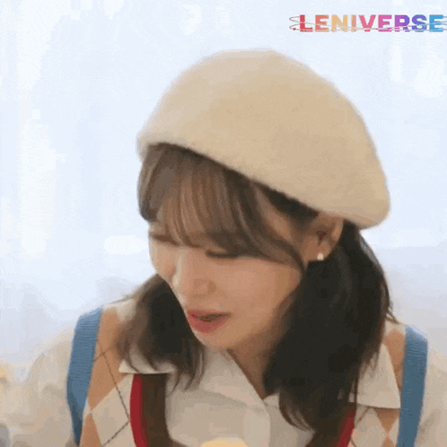 a girl wearing a white beret and a plaid vest is eating a banana .