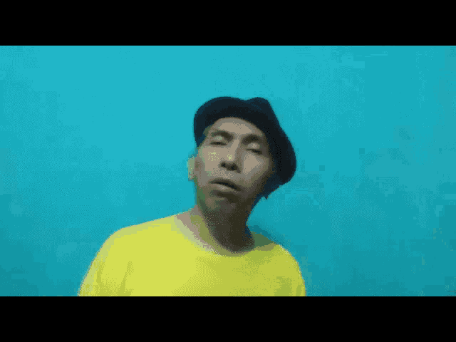 a man wearing a yellow shirt and a hat is making a funny face