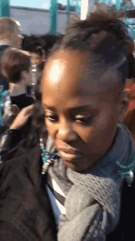 a girl with a scarf around her neck looks at the camera with a serious look on her face