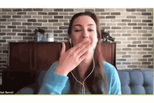 a woman wearing headphones is yawning while sitting on a couch in front of a brick wall .