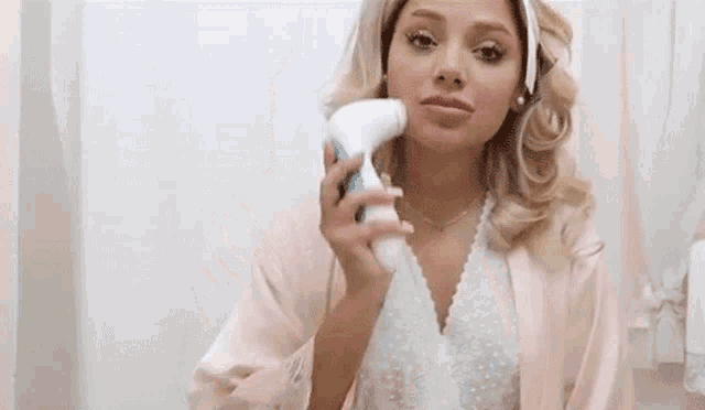a woman is using a facial cleansing brush on her face in a bathroom .