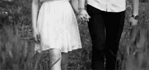 a black and white photo of a man and a woman holding hands while walking through a field .