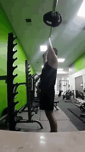 a man is lifting a barbell over his head in a gym .