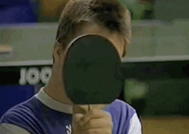 a young man is holding a ping pong paddle in front of his face and giving the middle finger .