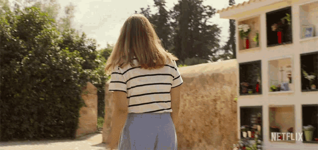 a woman walking in front of a cemetery with a netflix logo on the bottom right