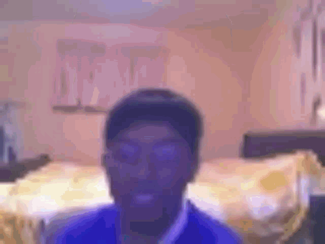 a blurry picture of a man in a blue shirt standing in a bedroom .