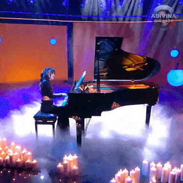 a woman is playing a piano on a stage with candles around it