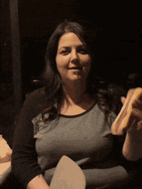 a woman in a grey shirt is holding a hot dog in her hand