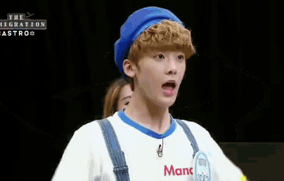 a boy wearing a blue hat and overalls is making a funny face .