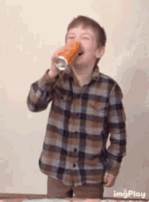 a young boy in a plaid shirt is drinking from a glass .