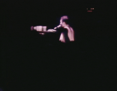 a man singing into a microphone on a stage in the dark