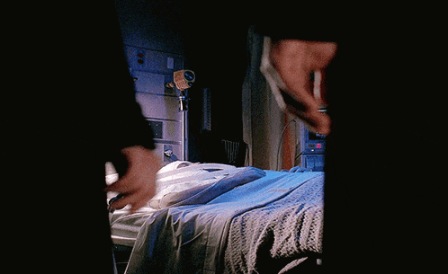 a person holding a knife in a dark room with a bed in the background