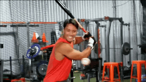 a man in a red tank top is swinging a baseball bat .