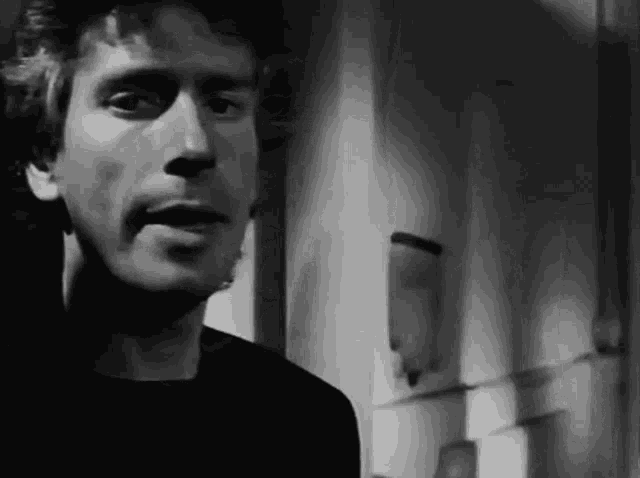 a black and white photo of a man standing next to a door .