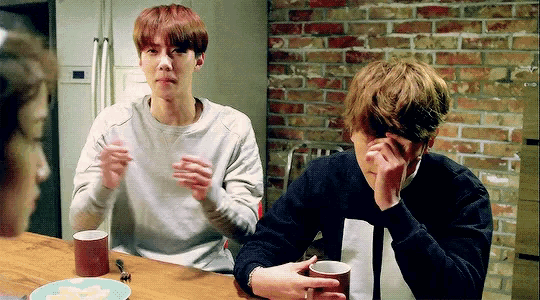 two young men are sitting at a table with a plate of food and a cup of coffee