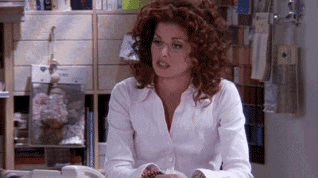 a woman with red hair is sitting at a desk with a telephone