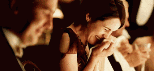 a woman is laughing and crying while sitting in a crowd of people .