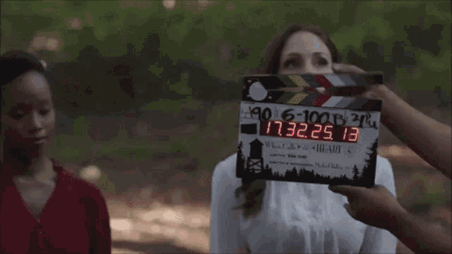 two women are standing next to each other in the woods and looking at something .