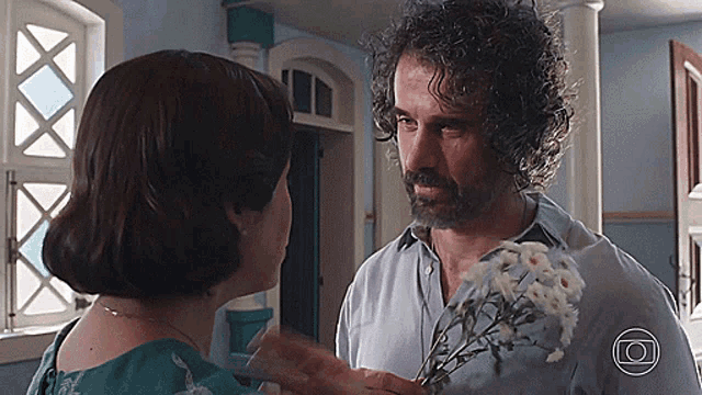 a man with curly hair is holding a bouquet of white flowers and looking at a woman
