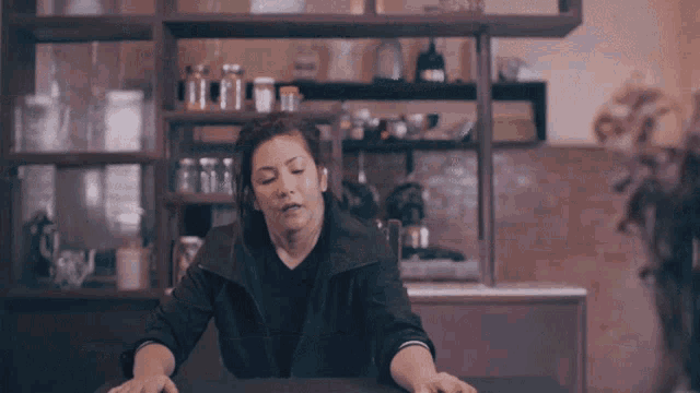 a woman sits at a table in a kitchen with her eyes closed
