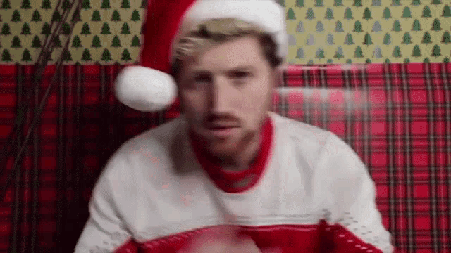 a man wearing a santa hat and sweater is sitting on a plaid couch .