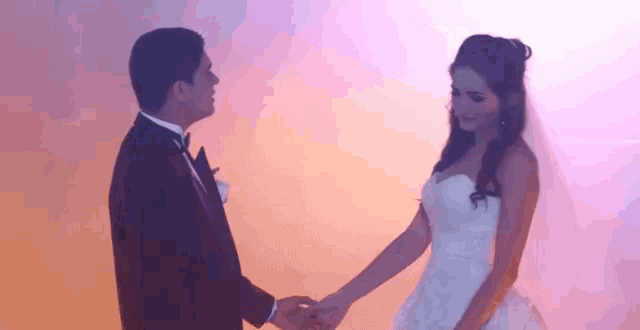 a bride and groom are holding hands while dancing in front of a pink background .
