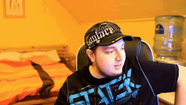 a man wearing a hat and a shirt that says ' eae ' on it sits in a chair