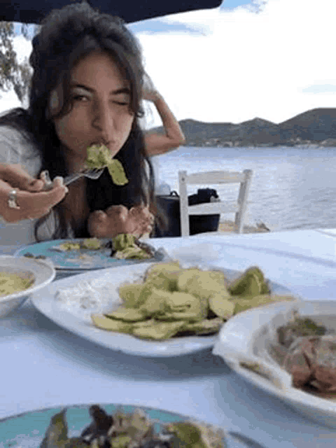 a woman is sitting at a table with plates of food and eating a salad .