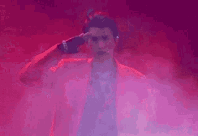 a man in a red jacket is holding a microphone in a pink fog .