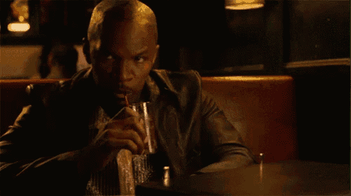 a man in a leather jacket is sitting at a table drinking a drink .