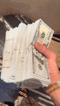 a hand holding a stack of hundred dollar bills