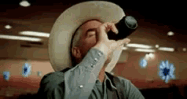 a man in a cowboy hat is drinking from a bottle in a diner .