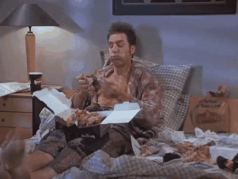 a man is sitting on a bed eating a box of chicken nuggets .