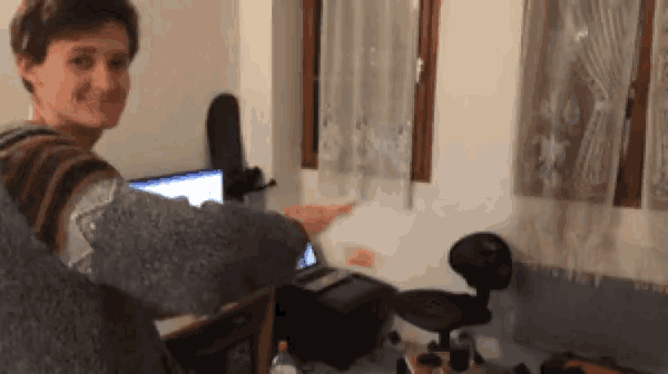 a man is standing in front of a desk with a laptop and a chair