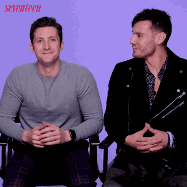 two men sit next to each other in front of a purple background with seventeen written on it