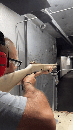 a man wearing a pair of red ear defenders is aiming a shotgun at a target
