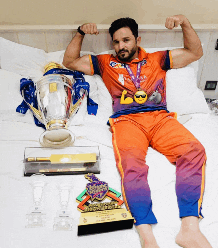 a man laying on a bed with trophies including a night riders trophy