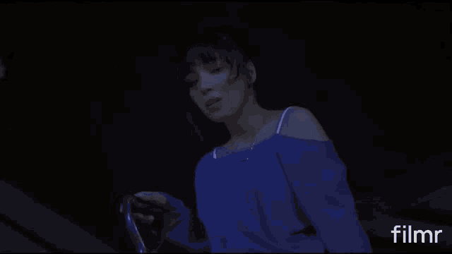 a woman in a blue off the shoulder top is standing in a dark room with filmr written on the bottom of the screen