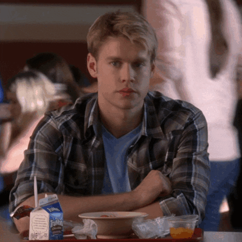a man in a plaid shirt sits at a table with a carton of toffano milk on it