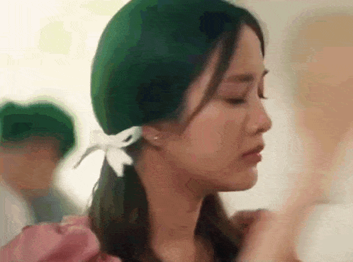 a woman wearing a green hat and a pink dress is standing in a room .