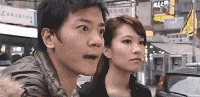 a man and a woman are standing next to each other on a street looking at something .
