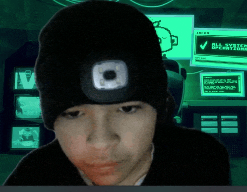 a person wearing a black beanie with a flashlight on their head in front of a screen that says all system operational