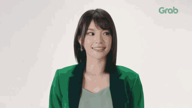 a woman in a green jacket stands in front of a grab ad