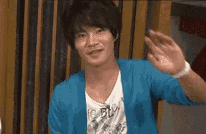 a young man in a blue cardigan is waving his hand .