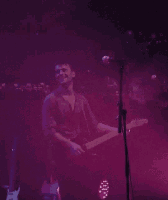 a man playing a guitar and singing into a microphone on stage