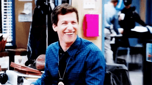 a man in a blue plaid shirt is sitting at a desk and smiling .