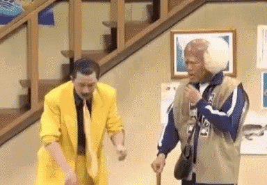 two men in yellow suits are standing next to each other on a stage . one man is holding a cane .